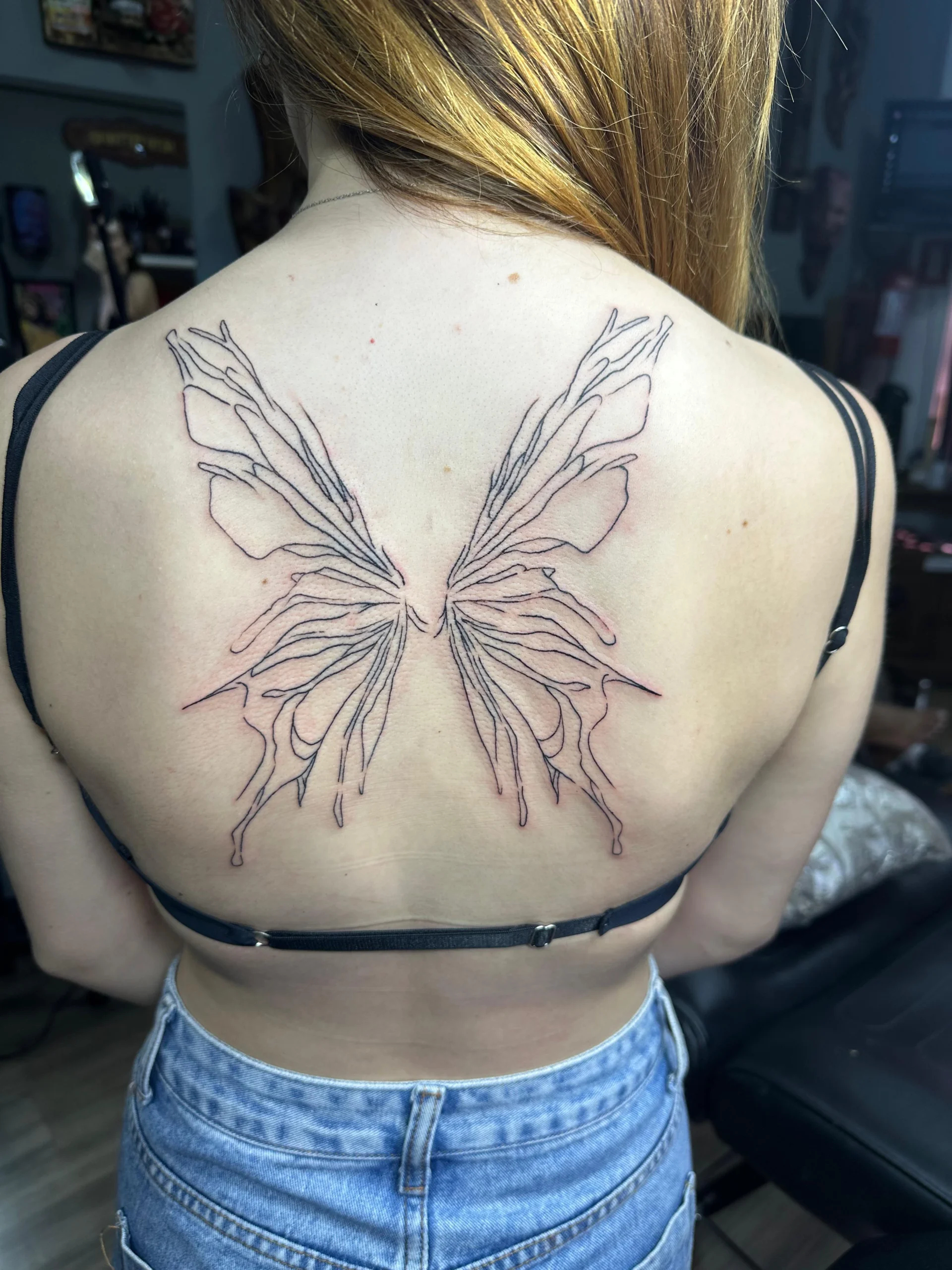 Abstract fine line butterfly tattoo on upper back artistic design Boca Raton studio