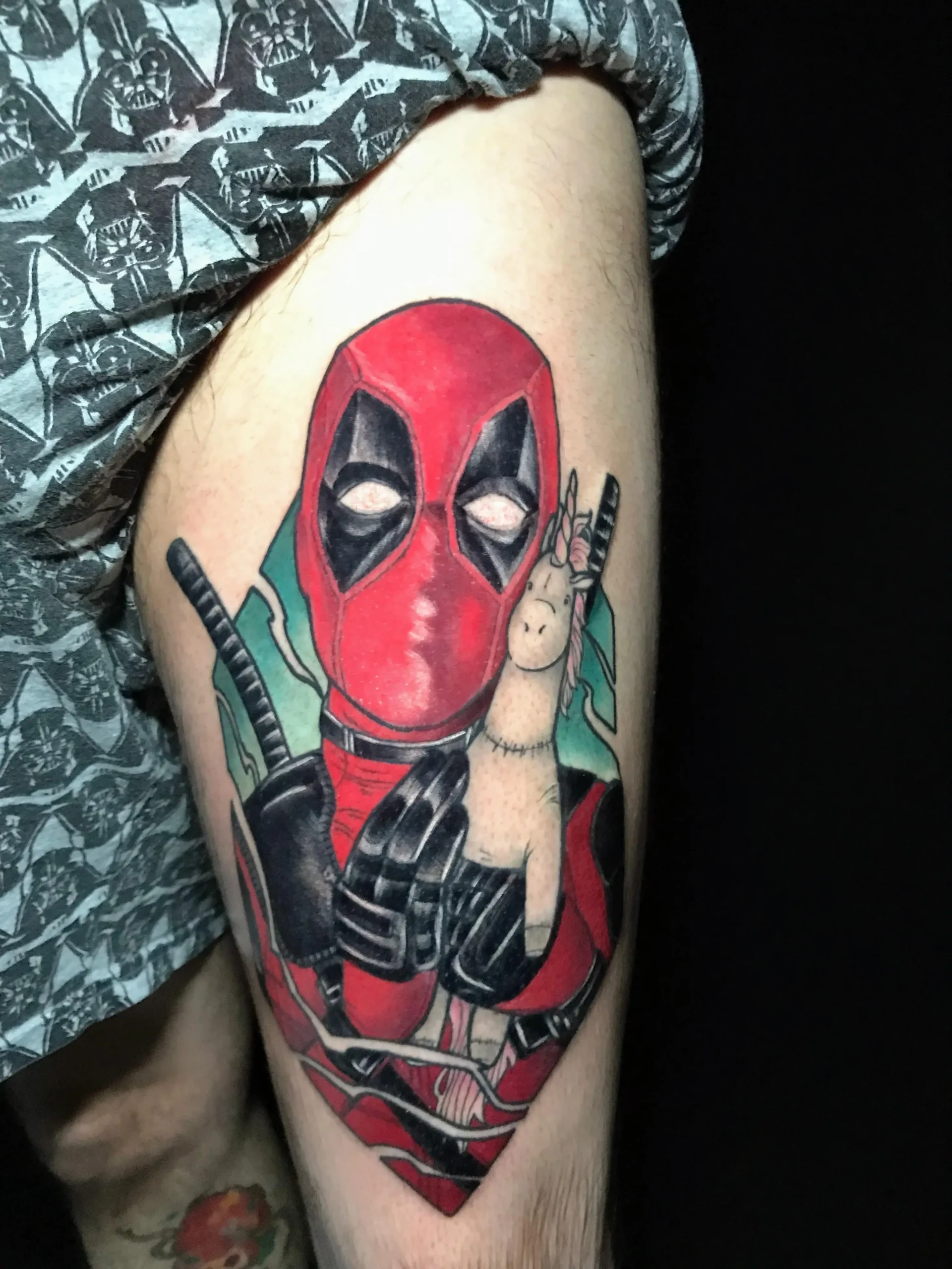 Funny Deadpool tattoo holding a unicorn plushie, vibrant Marvel comic book ink on the thigh, done in Boca Raton, Florida.