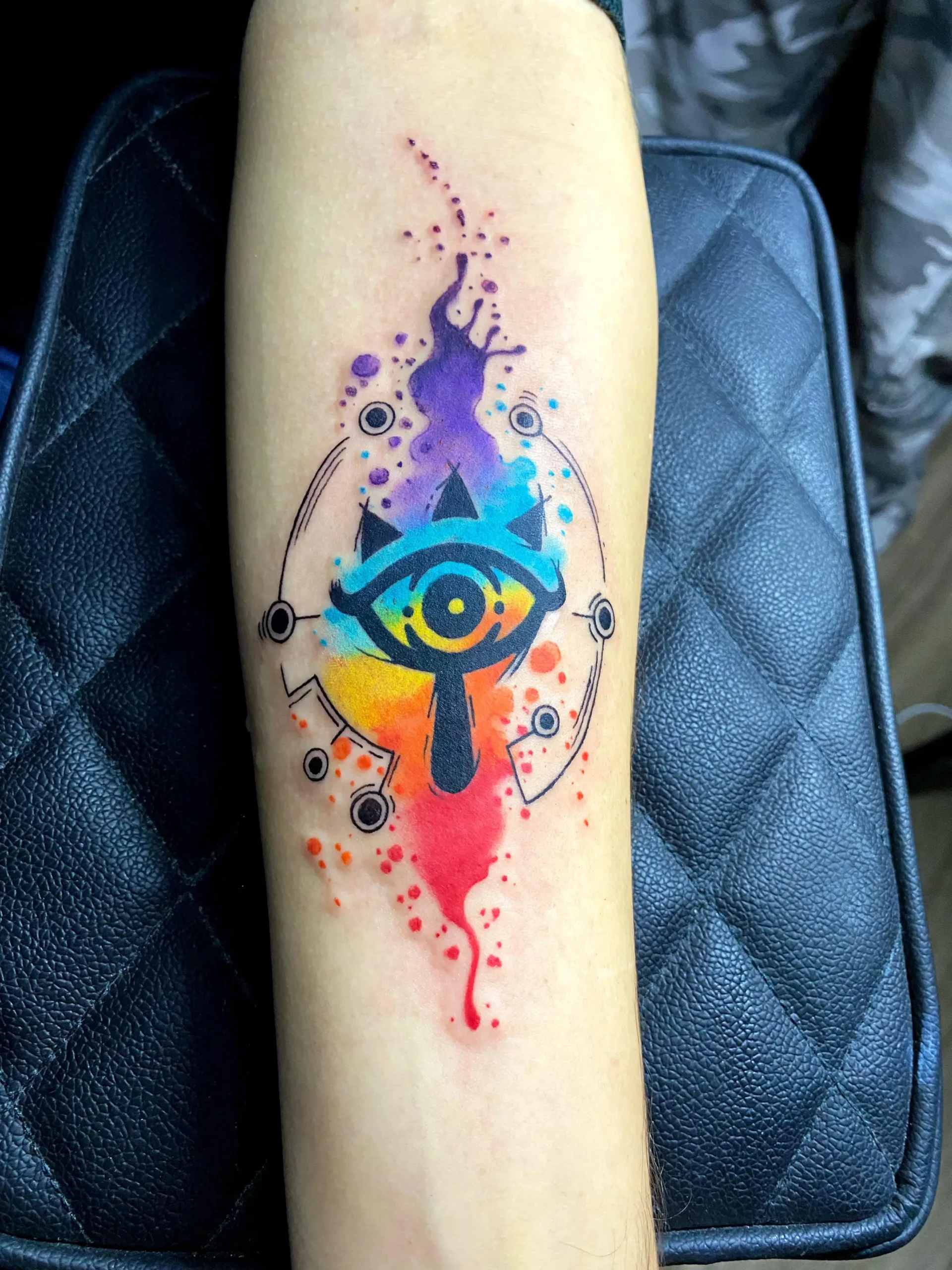 Watercolor Sheikah Eye symbol tattoo from Legend of Zelda, colorful gamer ink created by a custom artist in Boca Raton, Florida.