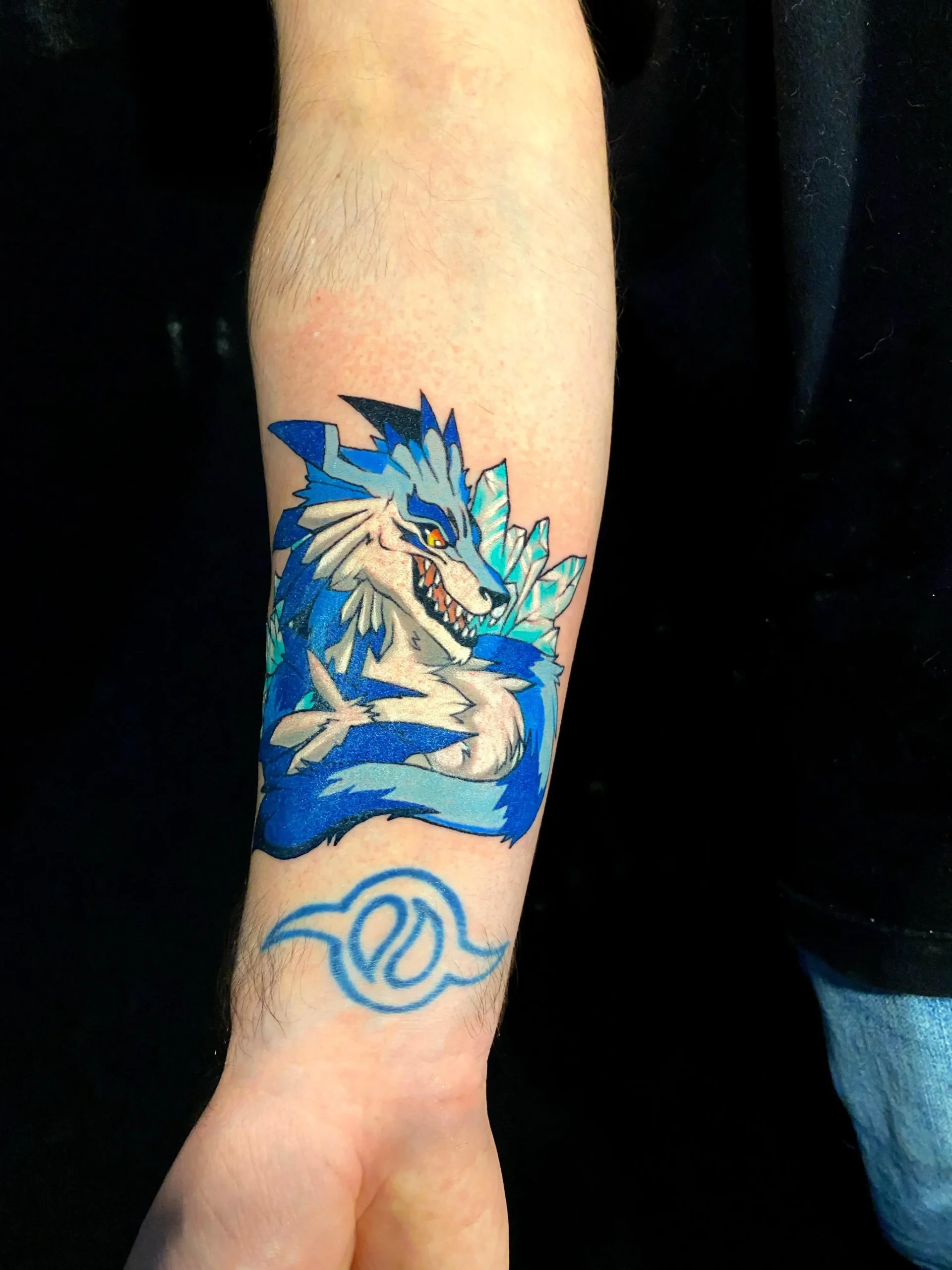 Blue anime wolf tattoo inspired by Digimon with crest symbol, vibrant cartoon ink for pop culture fans in Boca Raton, Florida.