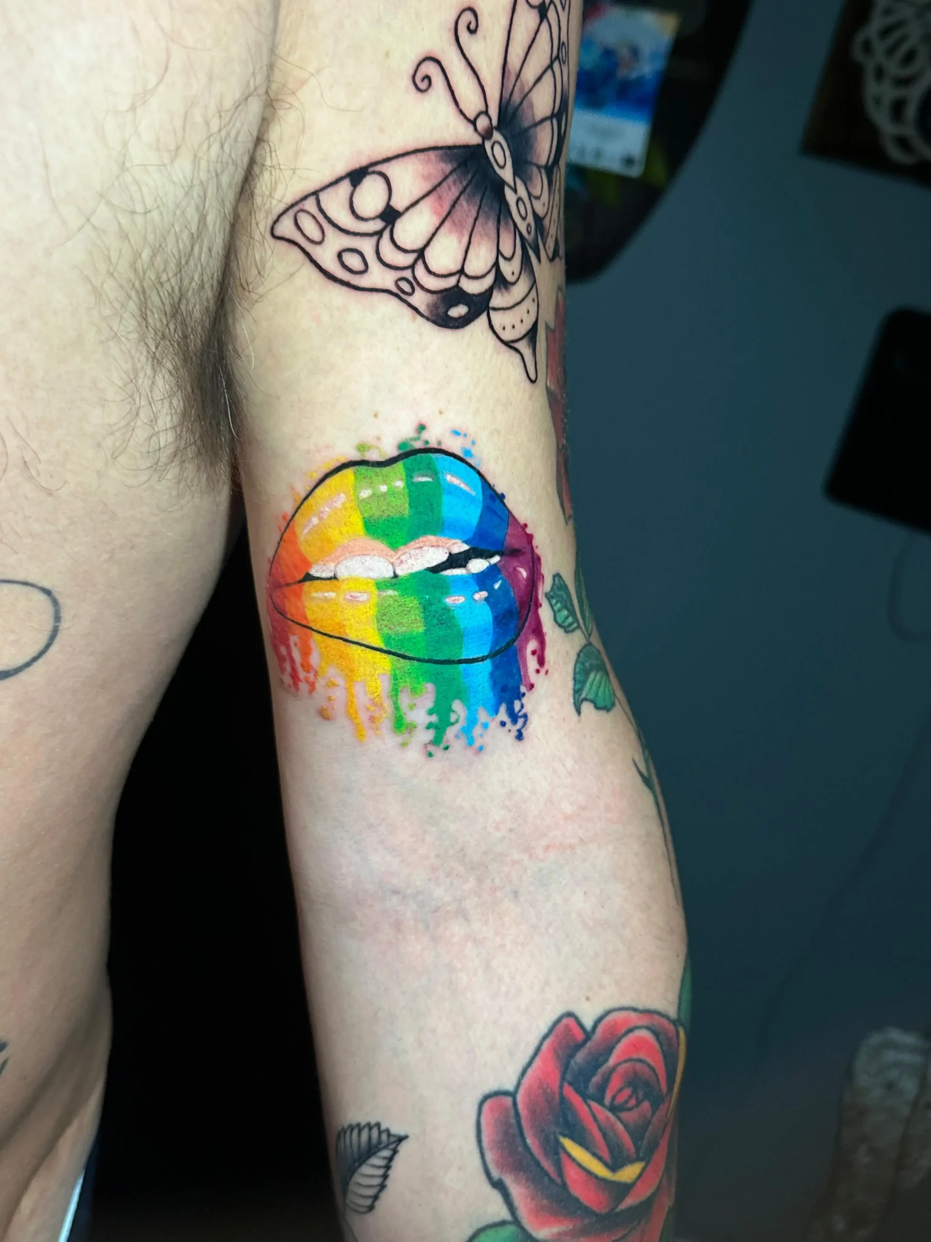 Vibrant watercolor lips tattoo with dripping rainbow colors and a butterfly, custom artistic ink by a creative tattoo shop in Boca Raton, Florida.