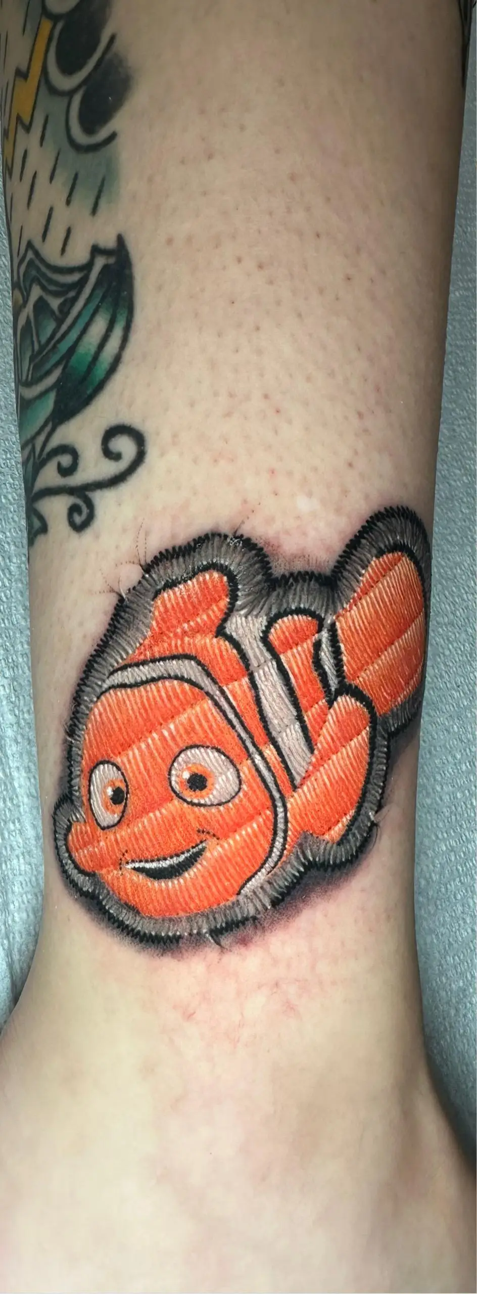 Nemo clownfish tattoo in realistic embroidery patch style on the ankle, detailed Disney Pixar fan art done in Boca Raton, Florida.