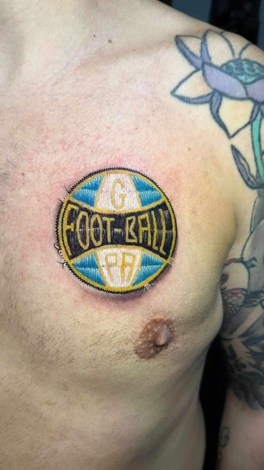 Realistic embroidery patch style tattoo of a soccer ball logo on the chest, detailed textured ink by a specialist in Boca Raton, Florida.