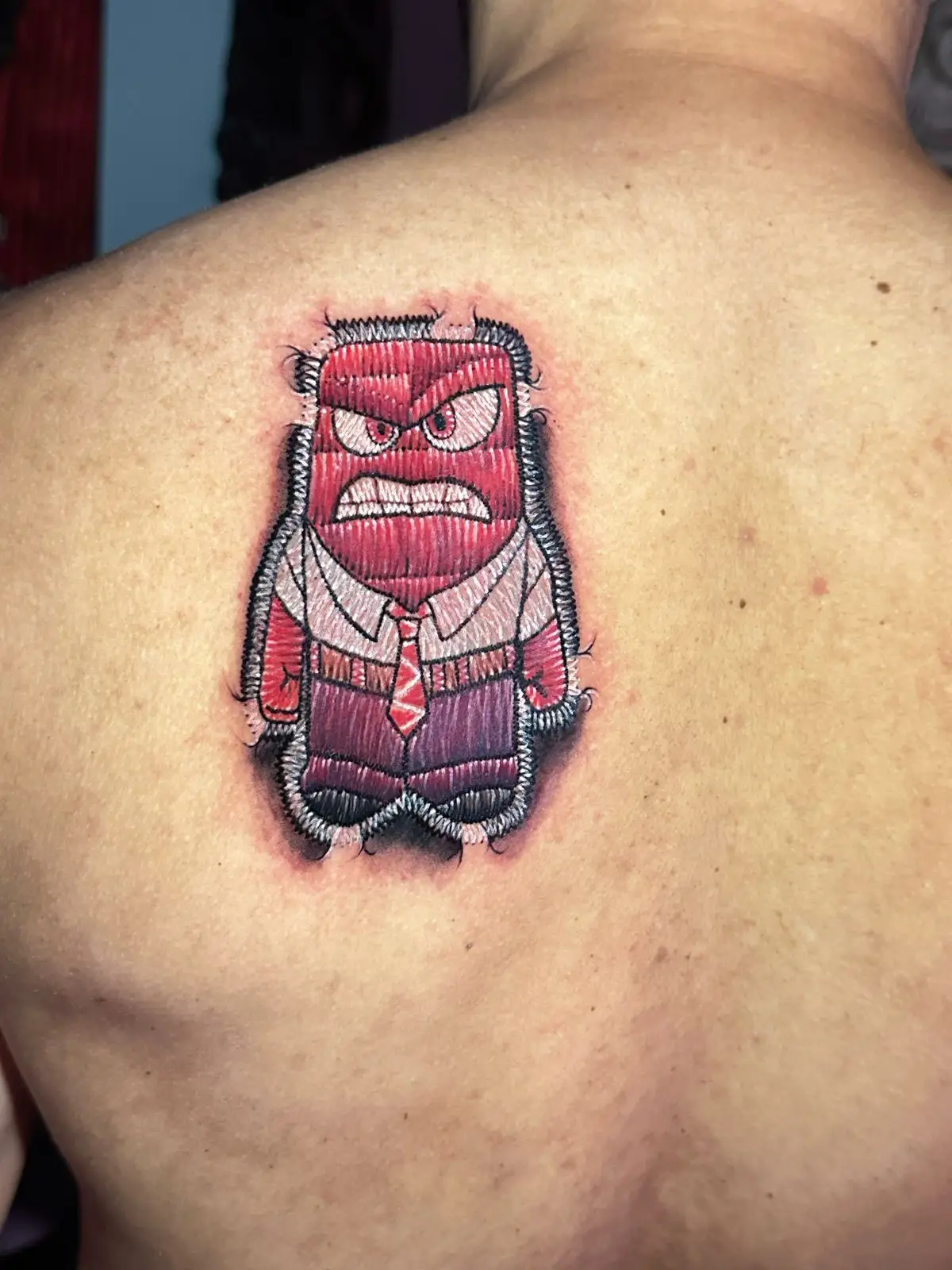 Anger character from Inside Out tattoo in embroidery patch style, realistic red texture ink on the back, created in Boca Raton, Florida.