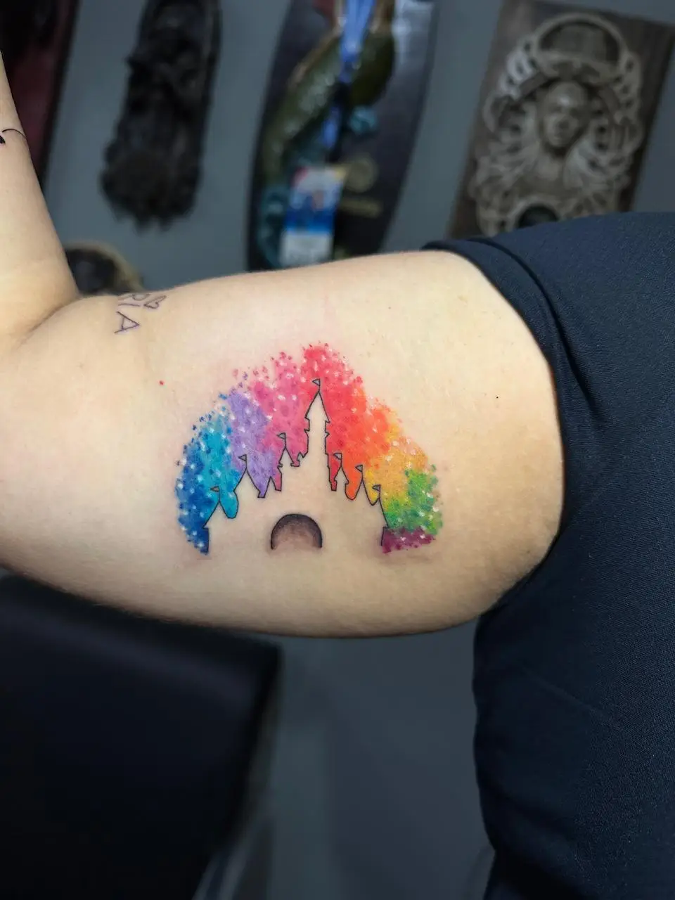 Disney castle silhouette tattoo with rainbow watercolor stippling on inner bicep Boca Raton tattoo studio