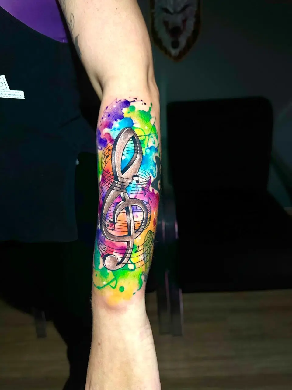 Watercolor treble clef music tattoo on forearm with colorful splashes by tattoo artist in Boca Raton FL