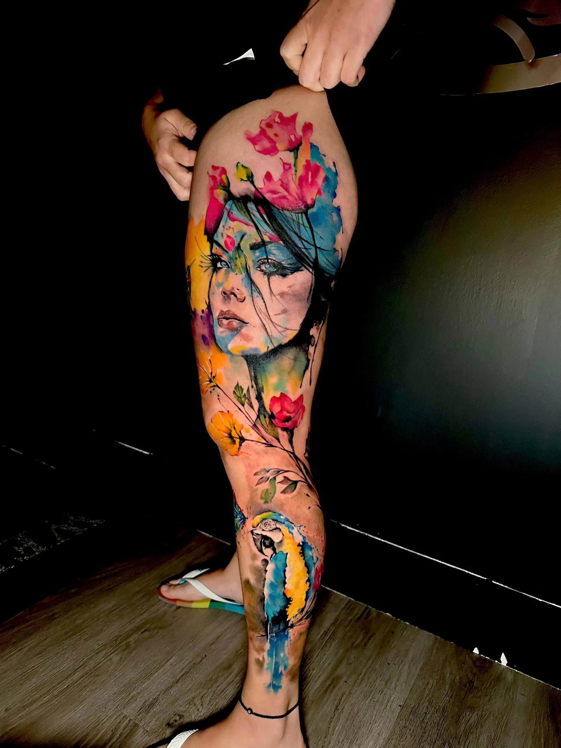 Watercolor macaw parrot tattoo detail on a leg sleeve, showing vibrant blue and yellow feathers, tropical ink in Boca Raton, Florida.