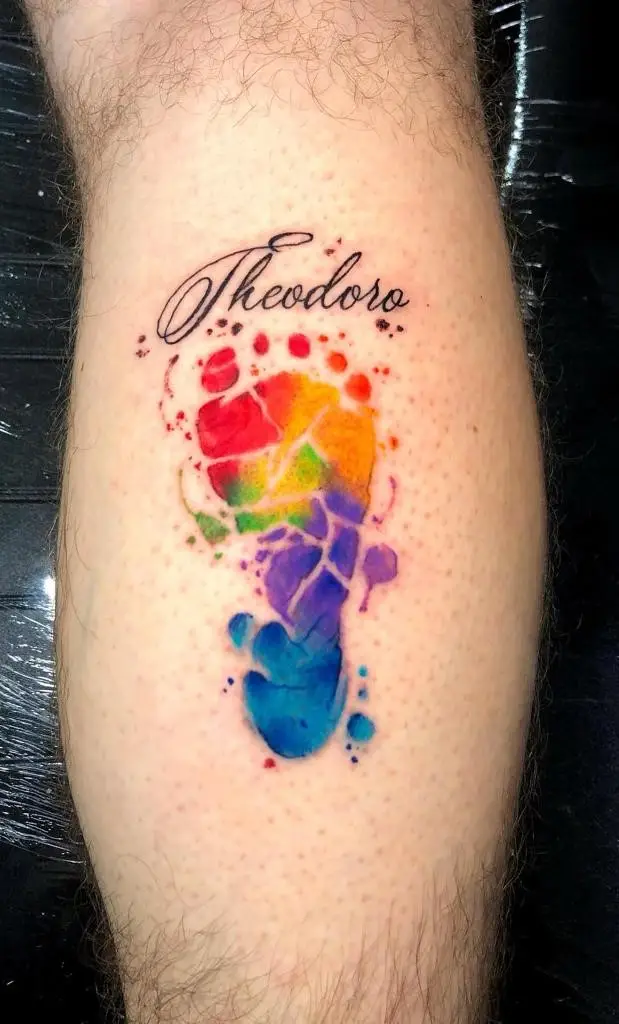 Rainbow watercolor baby footprint tattoo with the name Theodoro on the calf, vibrant memorial or birth tribute in Boca Raton, Florida.