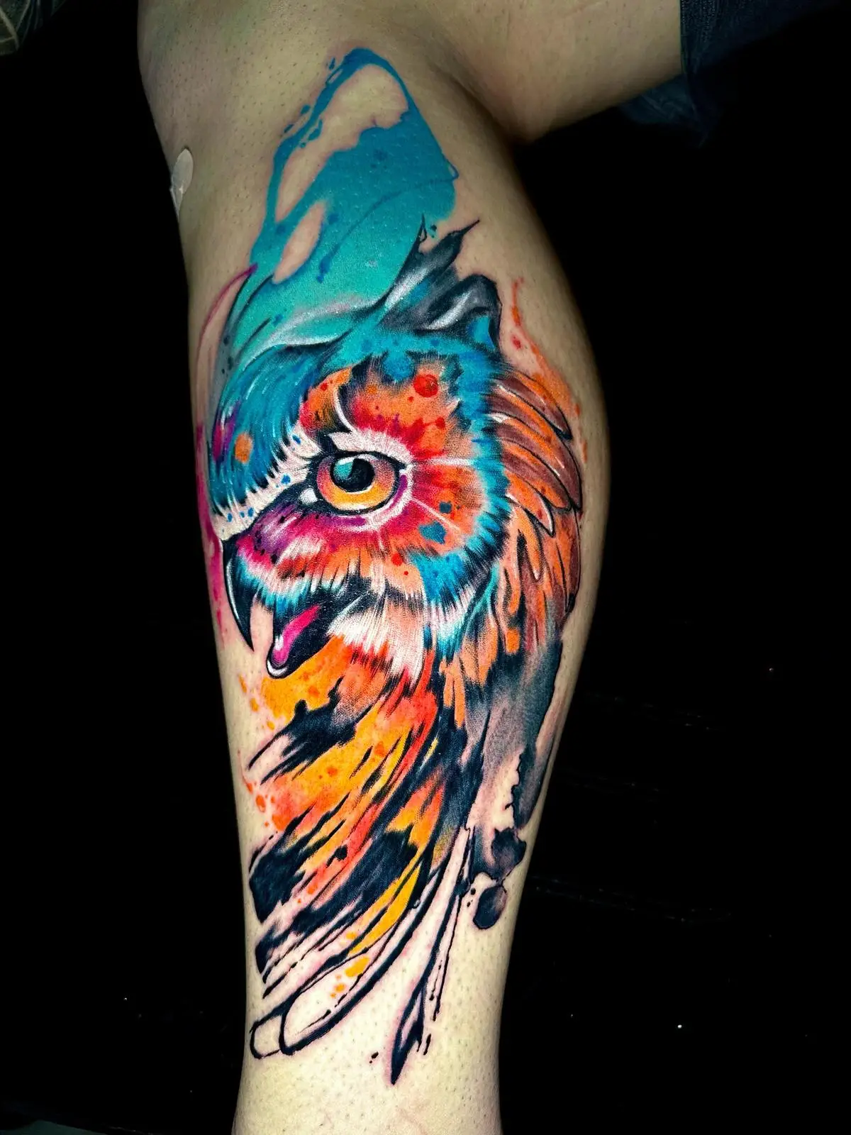 Vibrant watercolor owl head tattoo on the calf, featuring bold colors and artistic brush strokes, inked by a pro in Boca Raton, Florida.