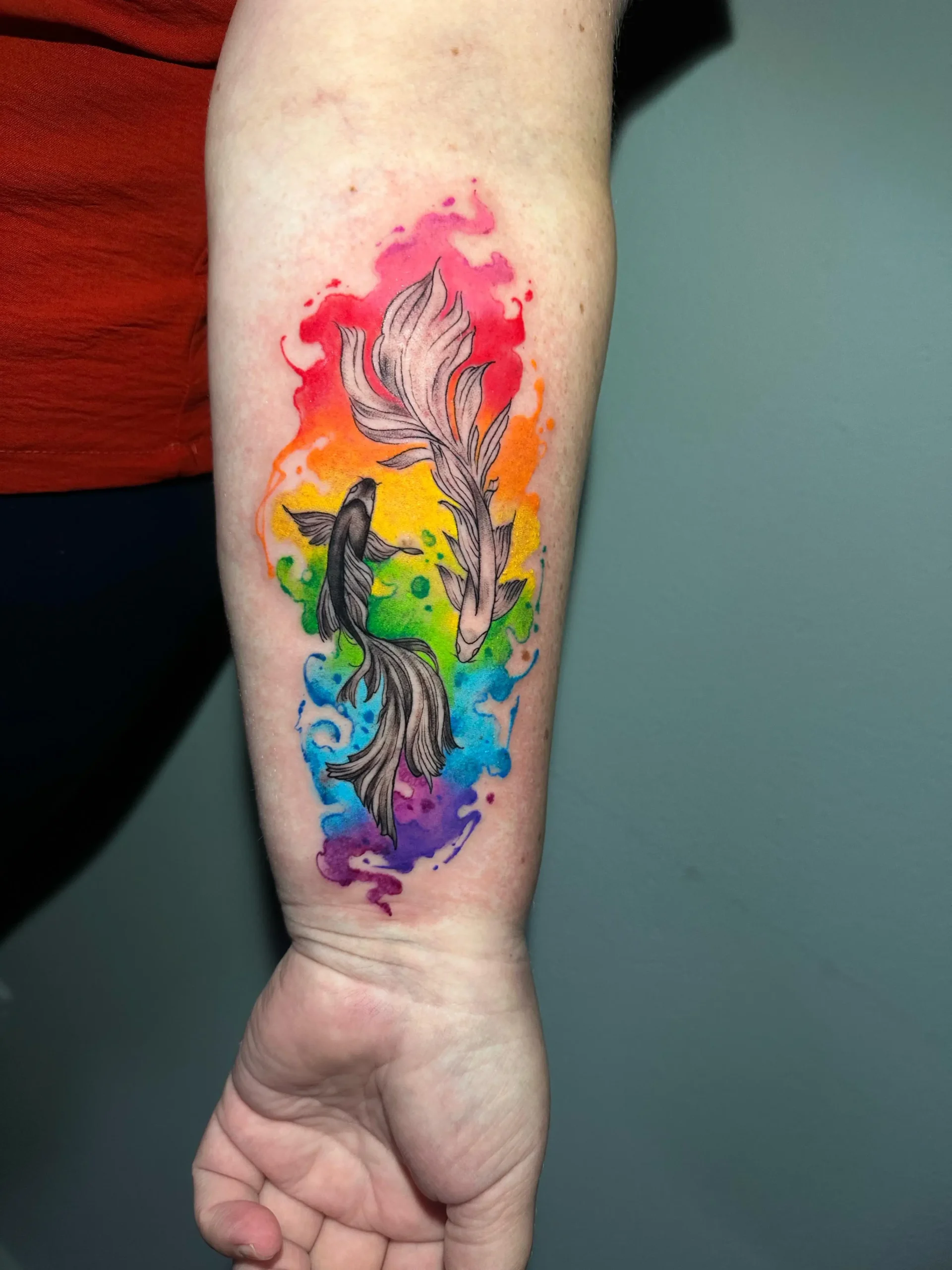 Pisces zodiac tattoo featuring two fish and a rainbow watercolor background on the forearm, colorful astrological ink in Boca Raton, Florida.