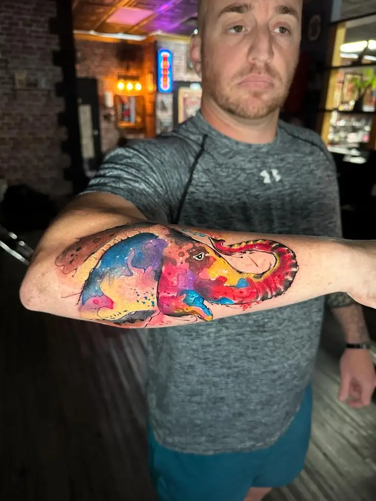 Abstract watercolor elephant tattoo on the forearm featuring galaxy colors and splatter effects, unique wildlife ink in Boca Raton, Florida.