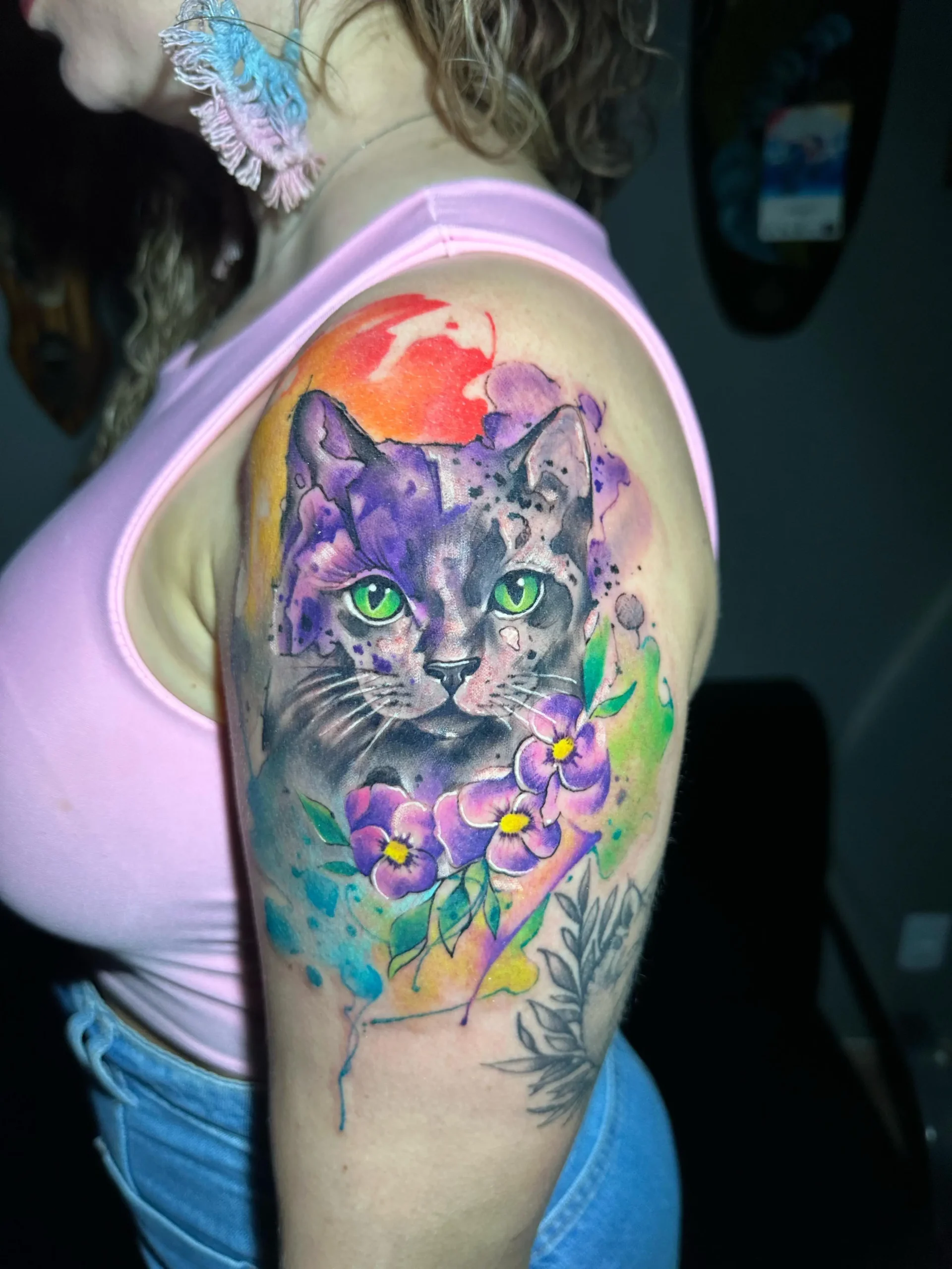 Watercolor cat portrait tattoo on the arm featuring purple and green floral elements, vibrant pet tribute ink by a Boca Raton artist.