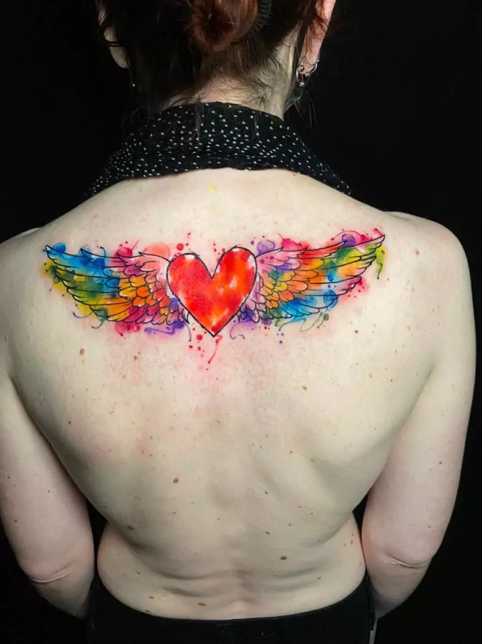 Colorful watercolor winged heart tattoo on the upper back, featuring vibrant rainbow wings, custom design by a top-rated tattoo artist in Boca Raton, Florida.