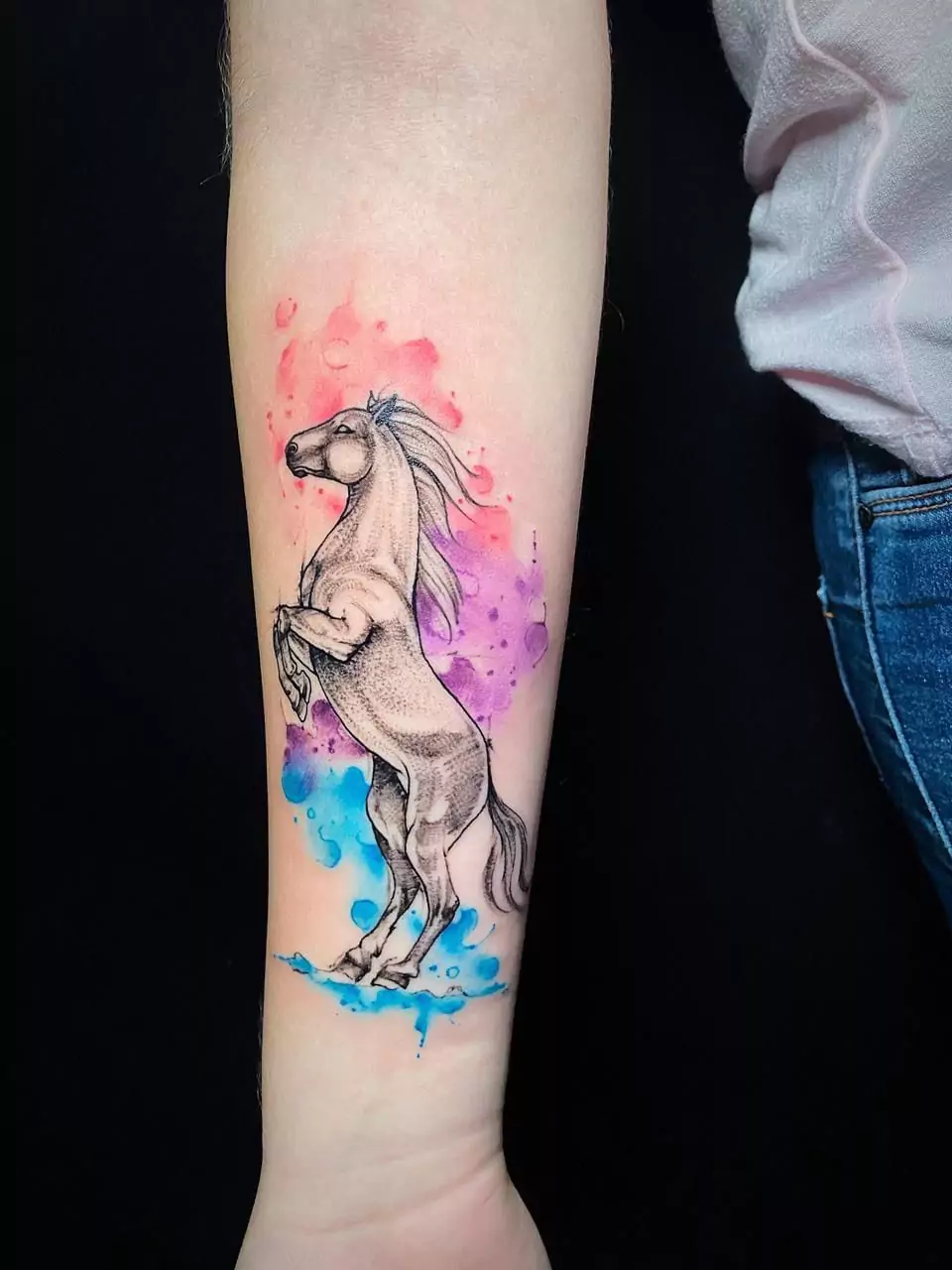 Sketch style horse tattoo with vibrant pink and blue watercolor splash background on the forearm, artistic ink by a tattoo artist in Boca Raton, Florida.
