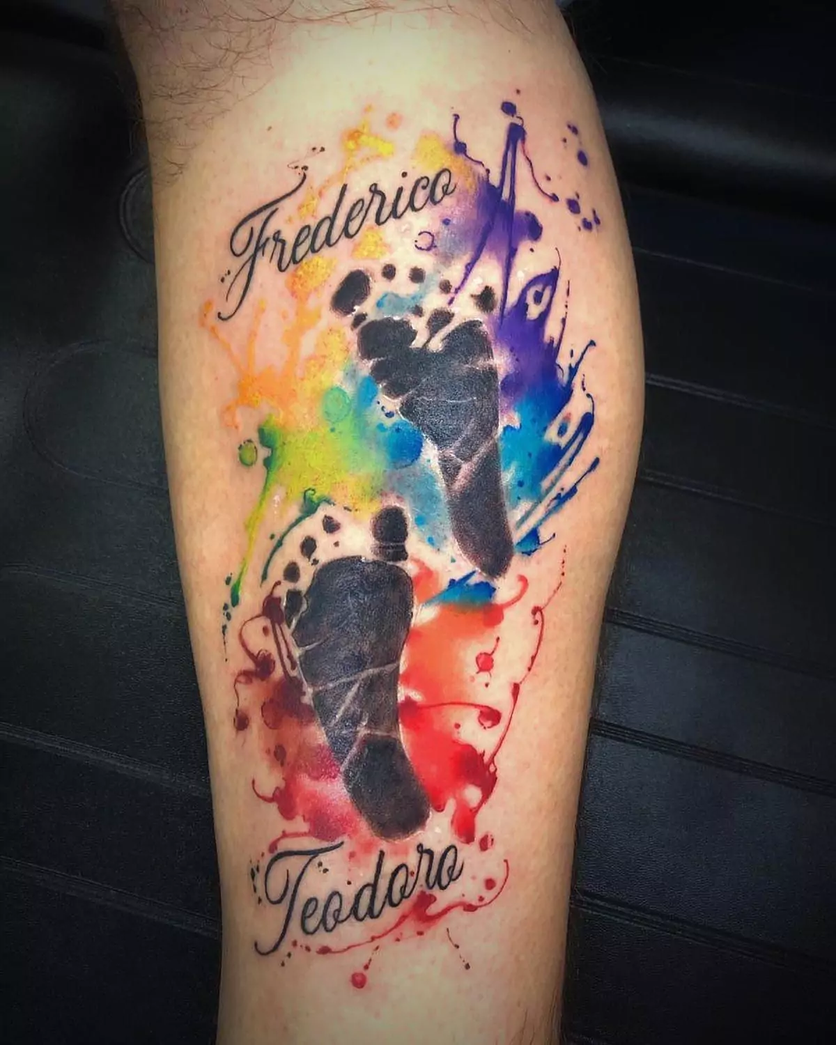 Custom watercolor baby footprints tattoo with script names Frederico and Teodoro on the calf, vibrant family tribute inked by a tattoo artist in Boca Raton, Florida.